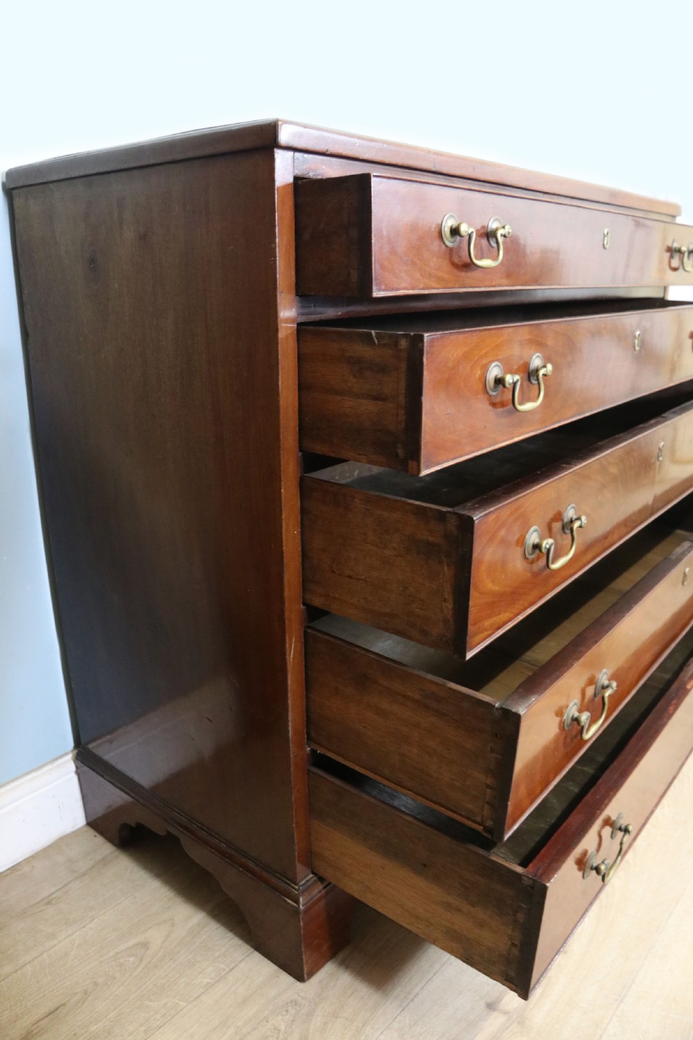 A 19th-century mahogany chest of drawers featuring five graduated drawers with brass swan-neck handles and bracket feet. View X