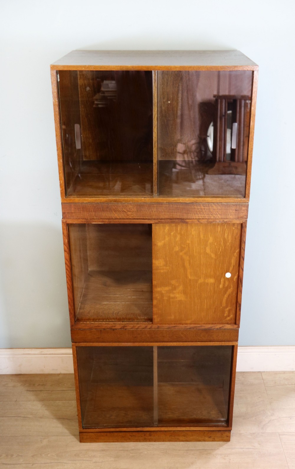 A three-tier mid-century oak sectional bookcase featuring sliding glass doors and a central section with a solid wood panel. View II