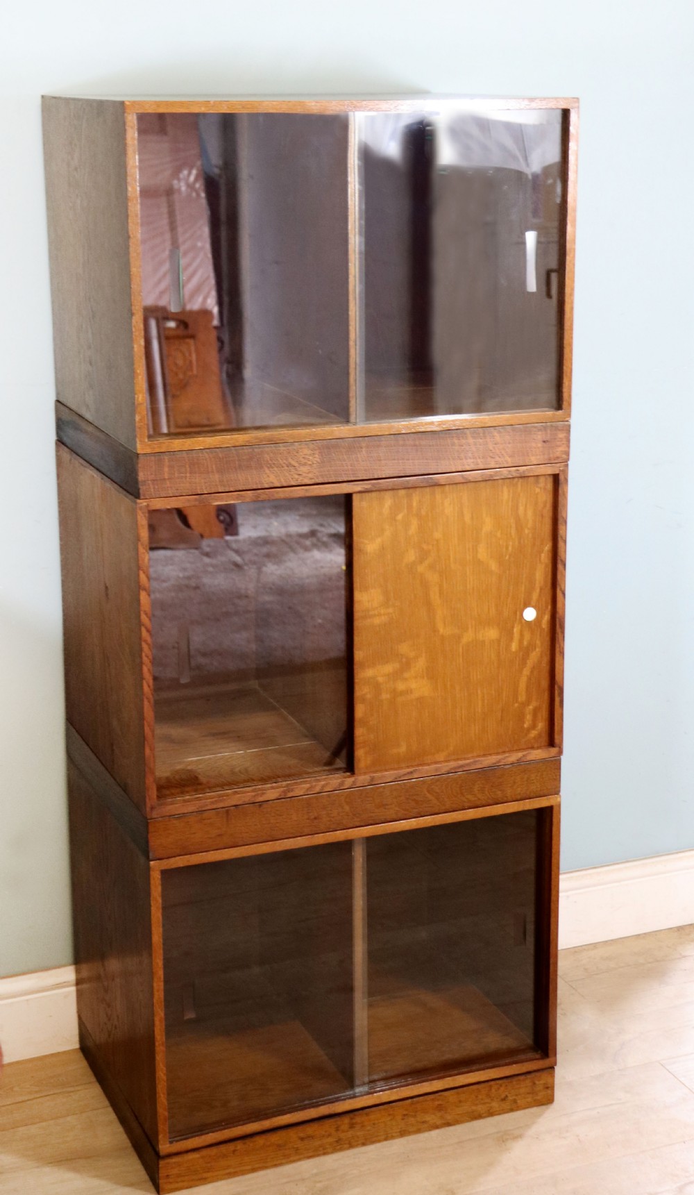 A three-tier mid-century oak sectional bookcase featuring sliding glass doors and a central section with a solid wood panel. View III