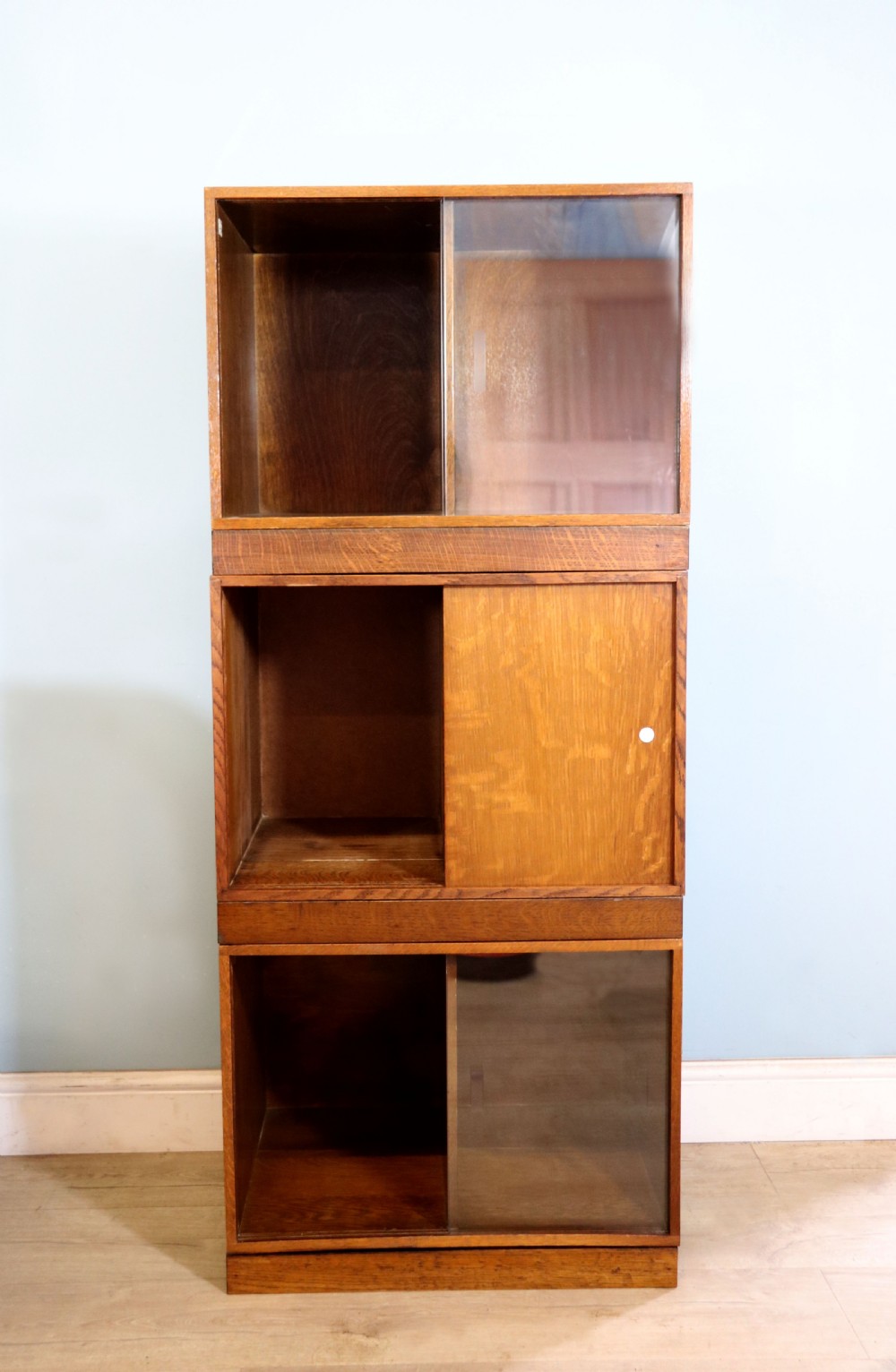 A three-tier mid-century oak sectional bookcase featuring sliding glass doors and a central section with a solid wood panel. View IV