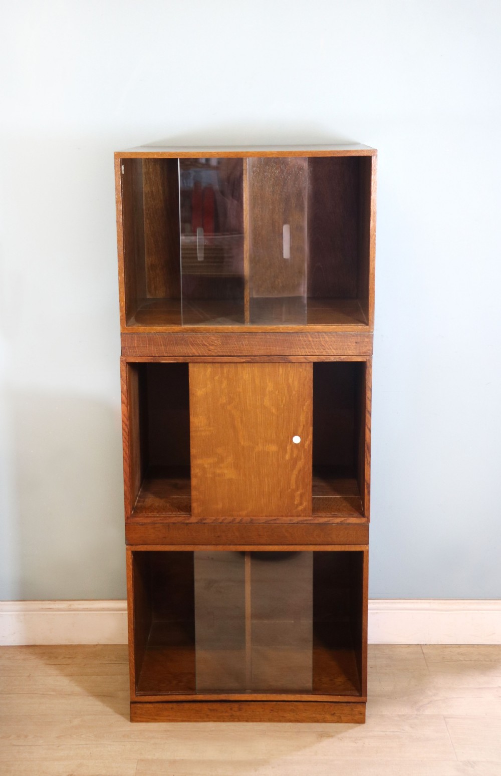A three-tier mid-century oak sectional bookcase featuring sliding glass doors and a central section with a solid wood panel. View V