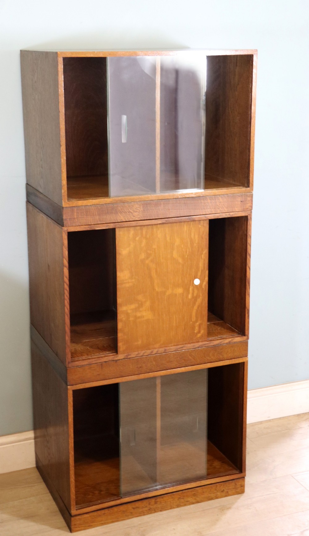 A three-tier mid-century oak sectional bookcase featuring sliding glass doors and a central section with a solid wood panel. View VI