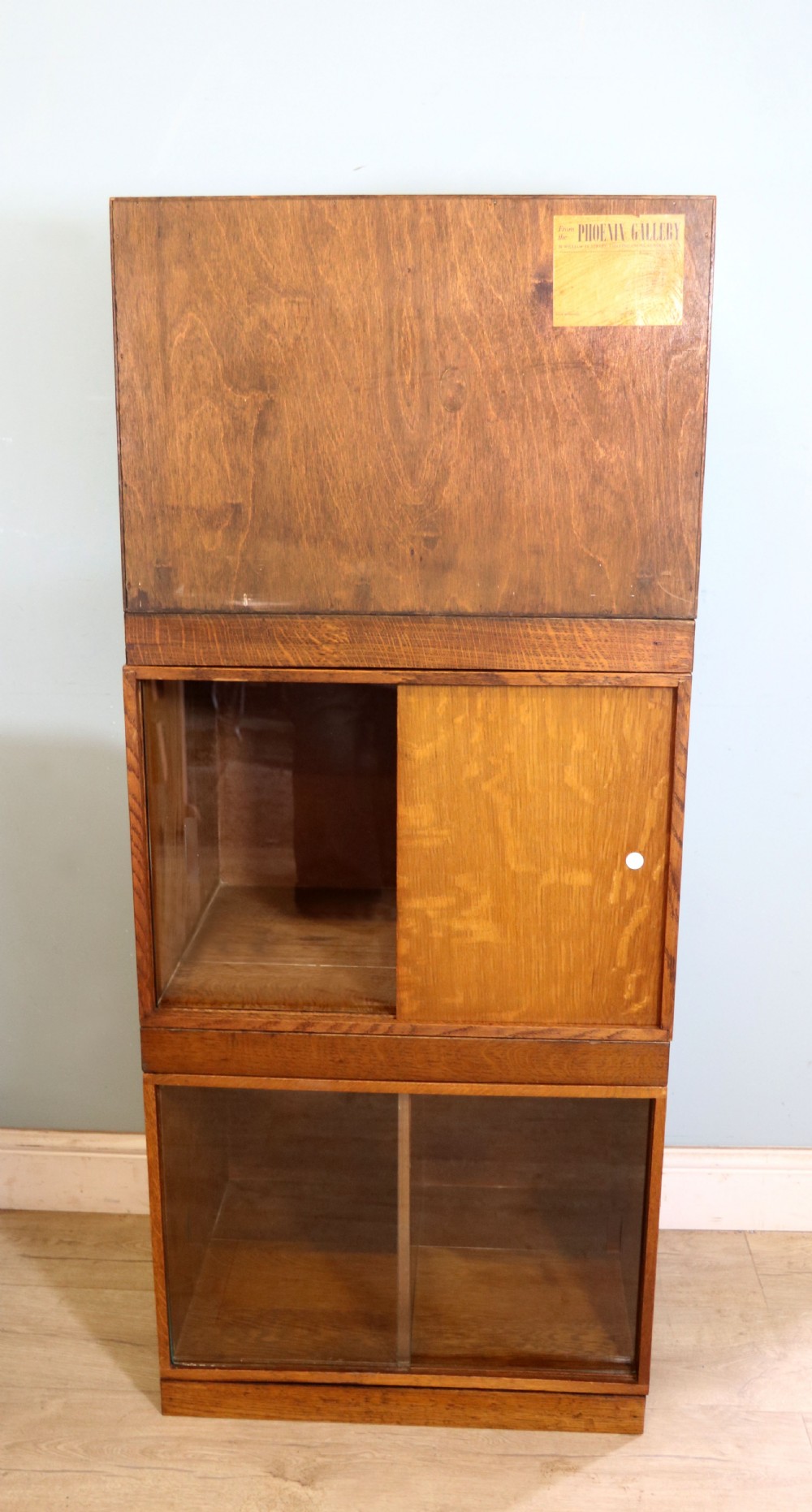 A three-tier mid-century oak sectional bookcase featuring sliding glass doors and a central section with a solid wood panel. View VII