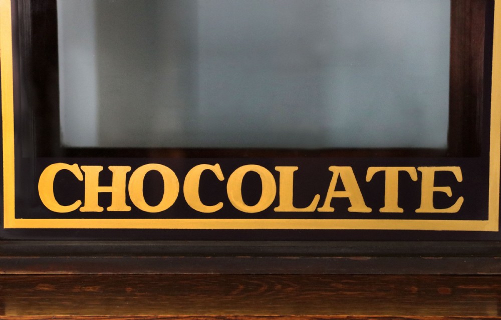 A dark hardwood rectangular shop display cabinet featuring gold lettering on the front glass pane reading Cadburys Dairy Milk Chocolate. View IX