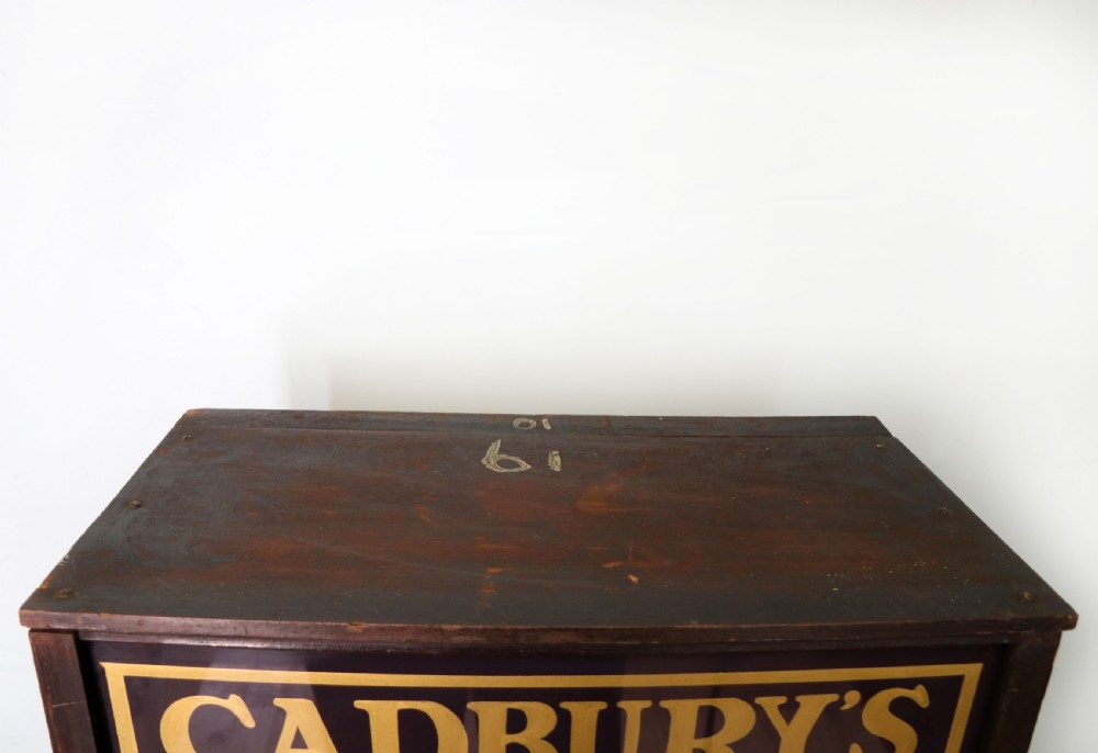 A dark hardwood rectangular shop display cabinet featuring gold lettering on the front glass pane reading Cadburys Dairy Milk Chocolate. View X