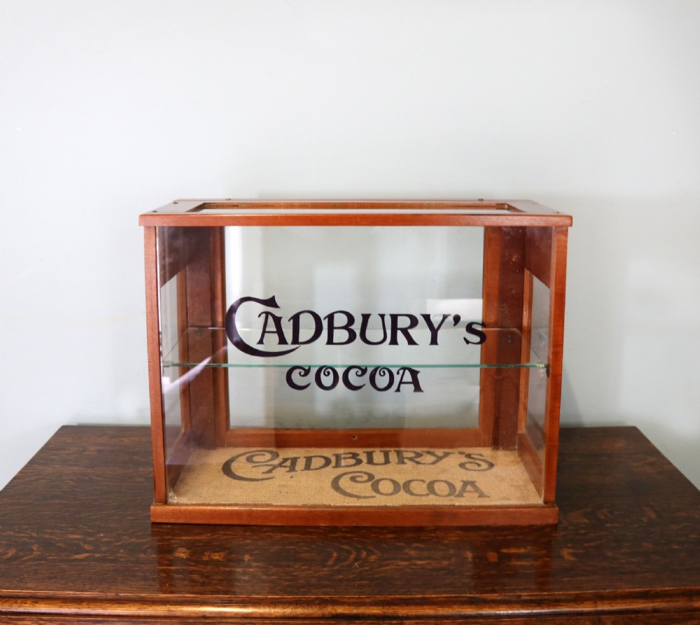 A glazed hardwood countertop display cabinet featuring Cadburys Cocoa typography printed on the front glass pane and inner base.