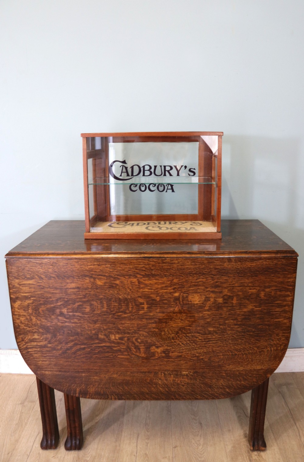 A glazed hardwood countertop display cabinet featuring Cadburys Cocoa typography printed on the front glass pane and inner base. View II