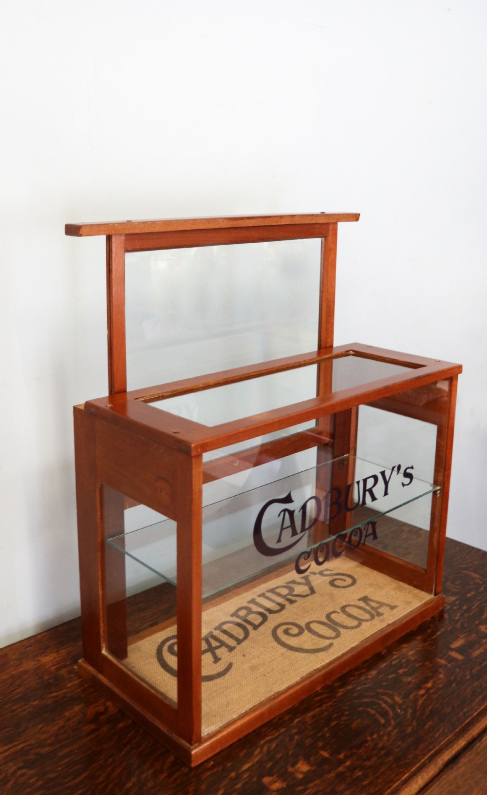 A glazed hardwood countertop display cabinet featuring Cadburys Cocoa typography printed on the front glass pane and inner base. View V