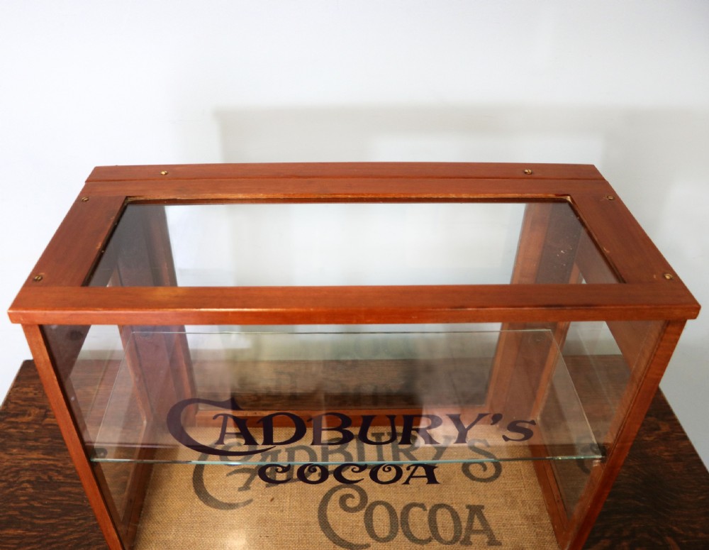 A glazed hardwood countertop display cabinet featuring Cadburys Cocoa typography printed on the front glass pane and inner base. View VII