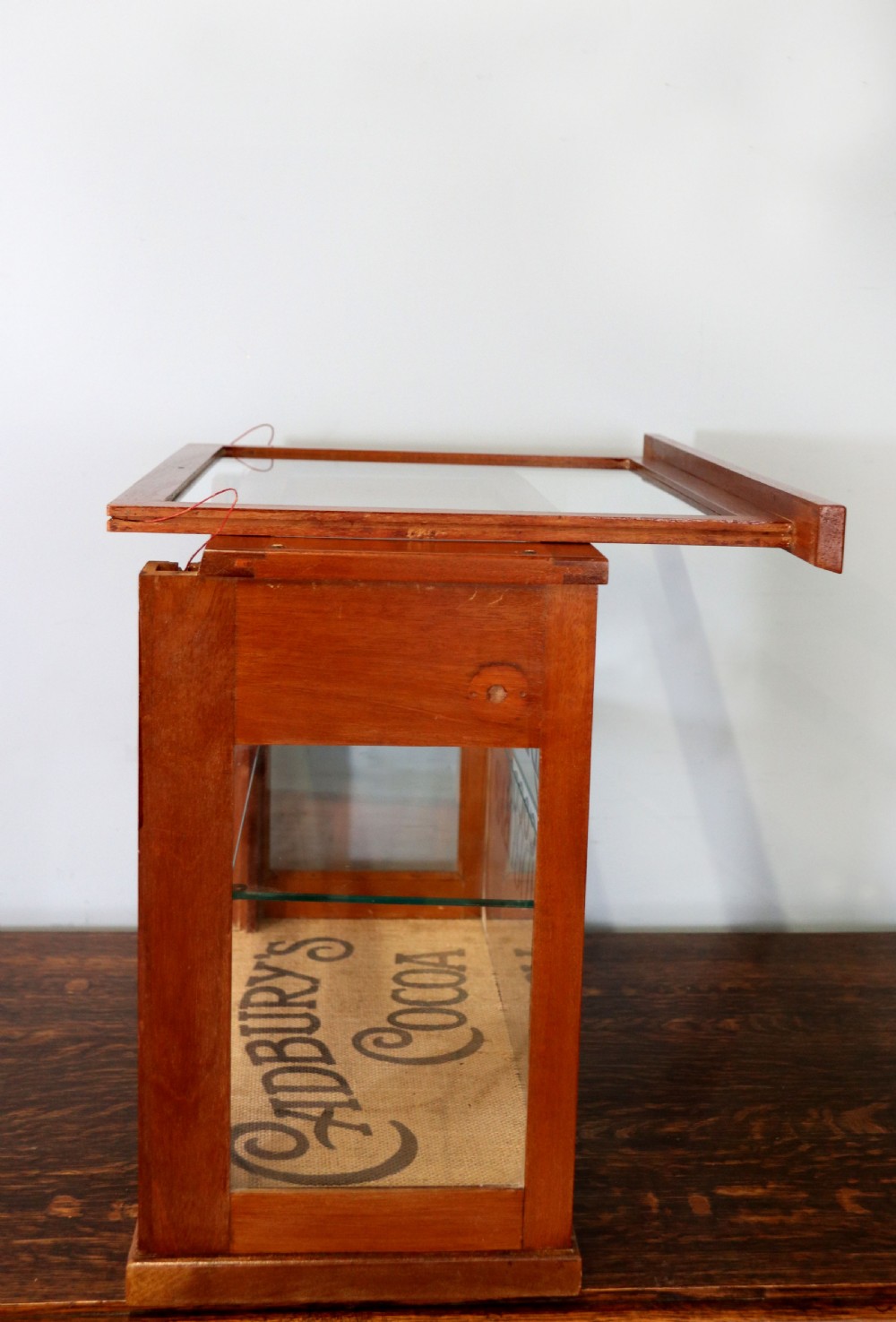 A glazed hardwood countertop display cabinet featuring Cadburys Cocoa typography printed on the front glass pane and inner base. View IX