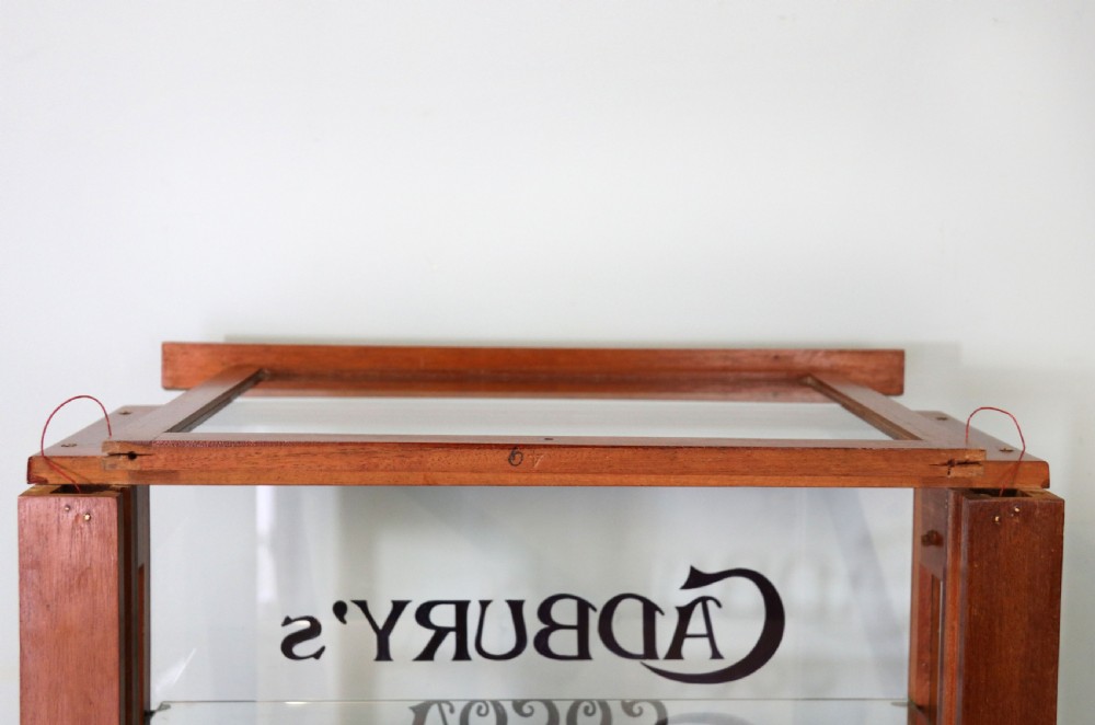 A glazed hardwood countertop display cabinet featuring Cadburys Cocoa typography printed on the front glass pane and inner base. View X