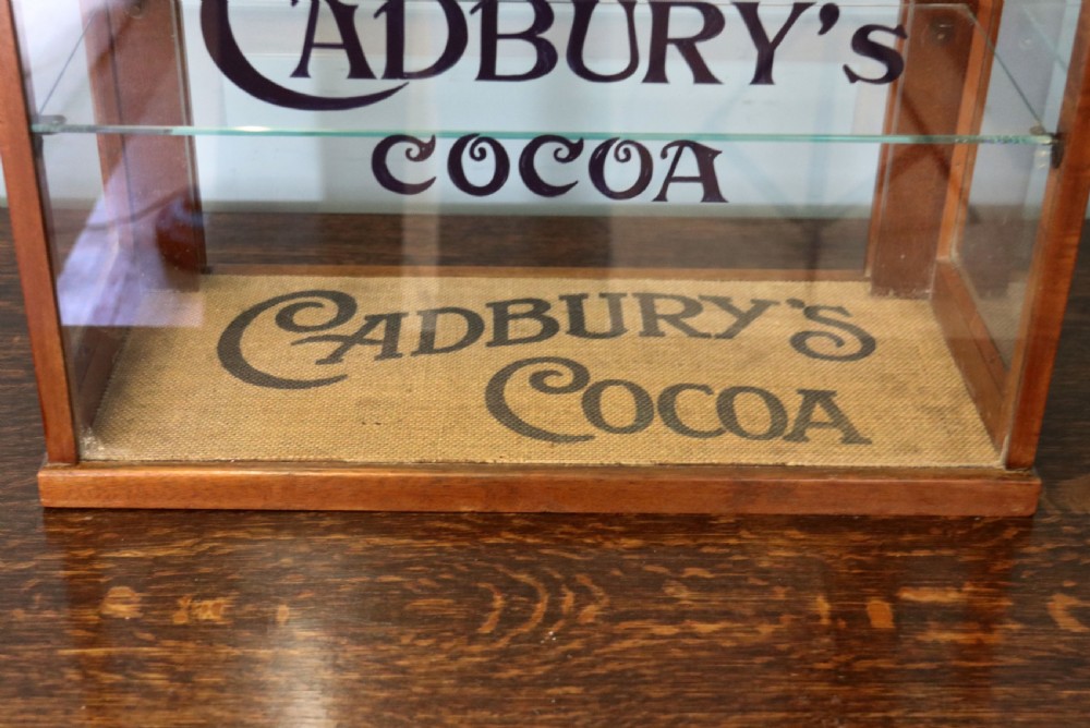 A glazed hardwood countertop display cabinet featuring Cadburys Cocoa typography printed on the front glass pane and inner base. View XIV