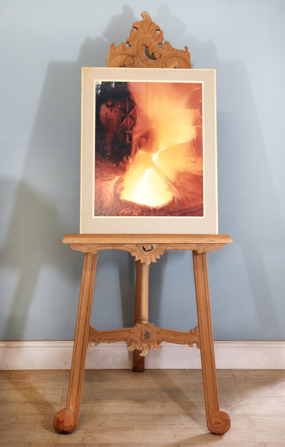 A mounted mid-century colour photograph depicting a foundry worker pouring molten metal.
