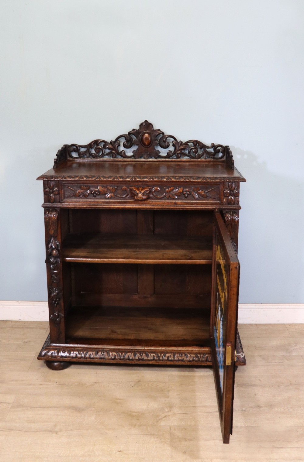 A dark carved oak side cabinet with a single glazed door displaying painted brewery signwriting and an ornate carved gallery back. View II