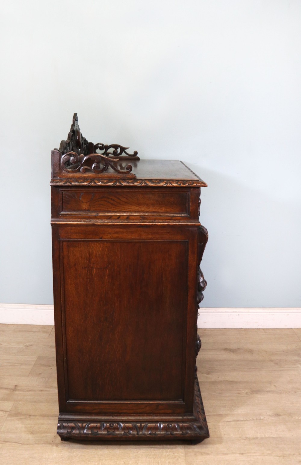 A dark carved oak side cabinet with a single glazed door displaying painted brewery signwriting and an ornate carved gallery back. View V