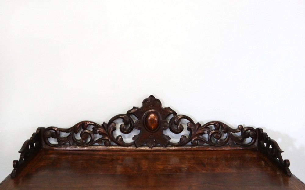 A dark carved oak side cabinet with a single glazed door displaying painted brewery signwriting and an ornate carved gallery back. View IX