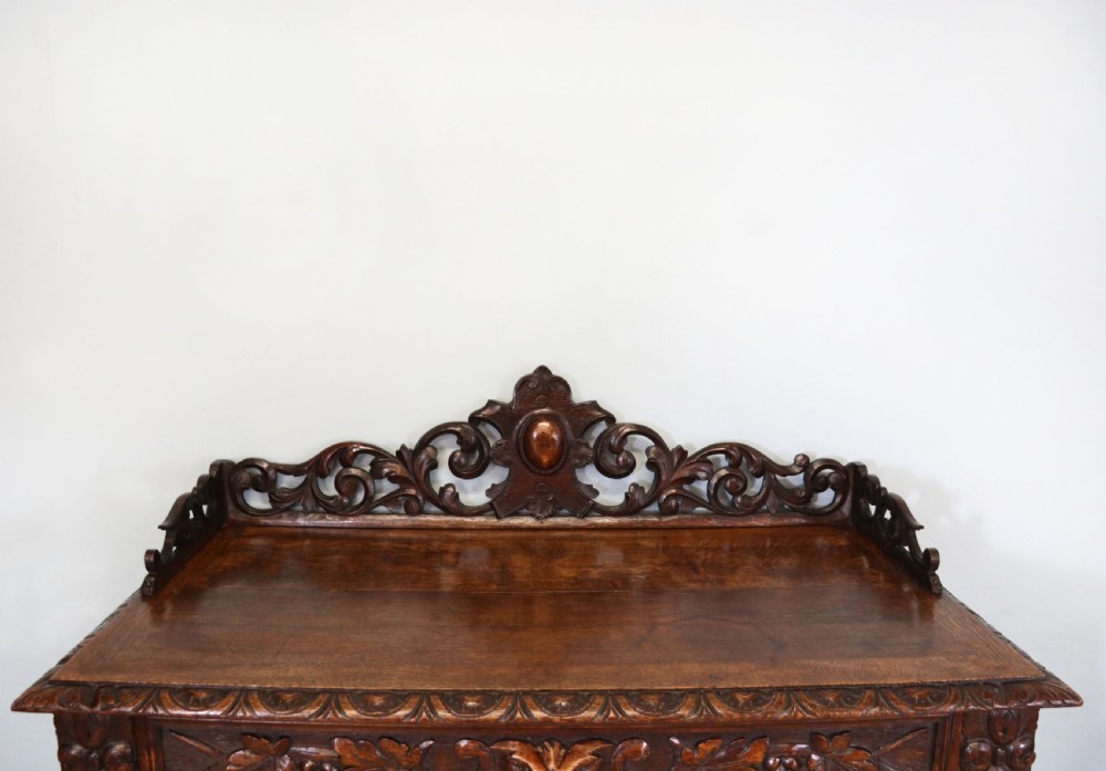 A dark carved oak side cabinet with a single glazed door displaying painted brewery signwriting and an ornate carved gallery back. View XI