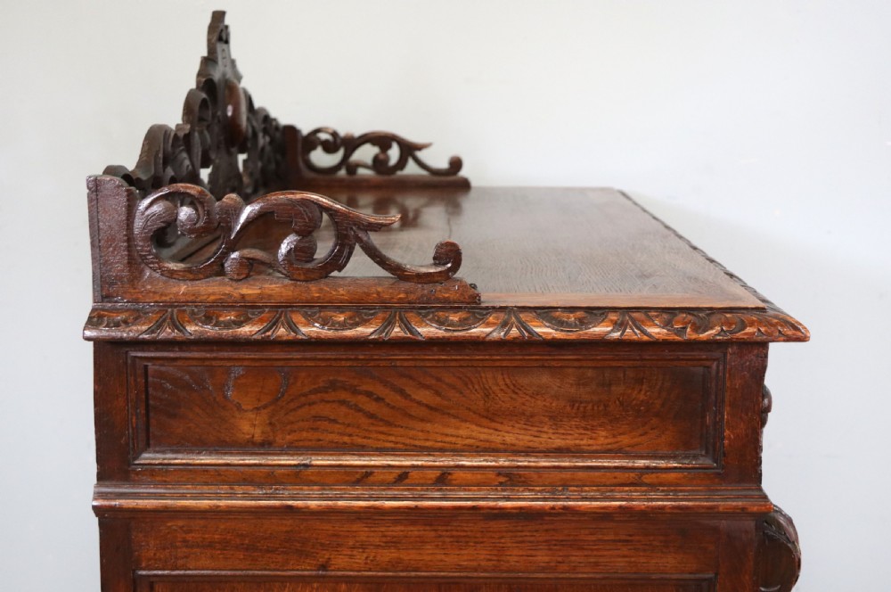 A dark carved oak side cabinet with a single glazed door displaying painted brewery signwriting and an ornate carved gallery back. View XV