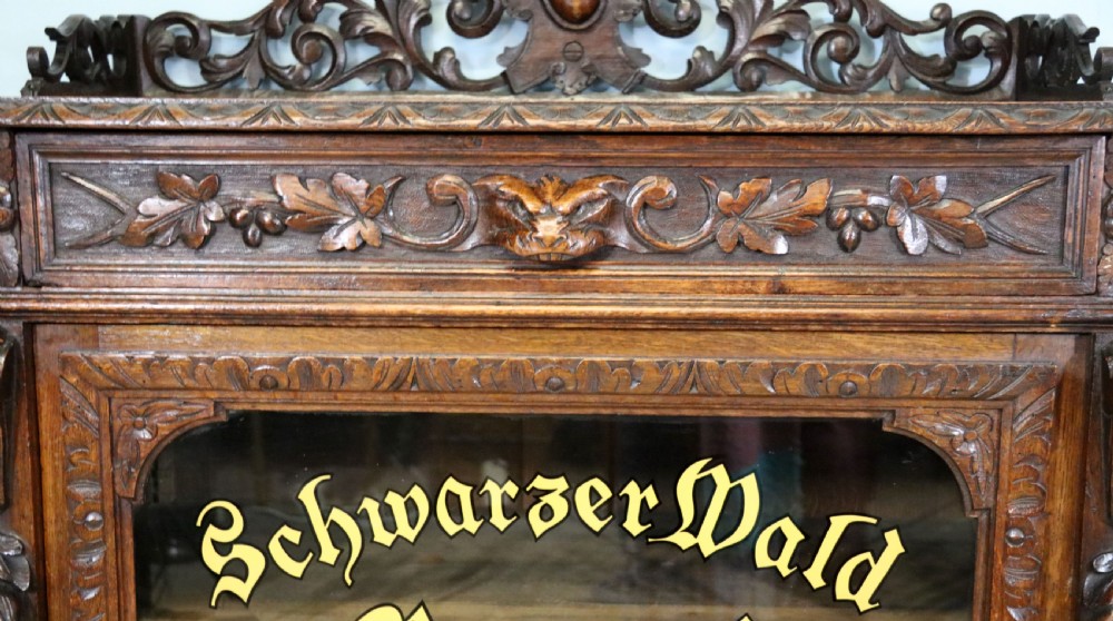 A dark carved oak side cabinet with a single glazed door displaying painted brewery signwriting and an ornate carved gallery back. View XXIII