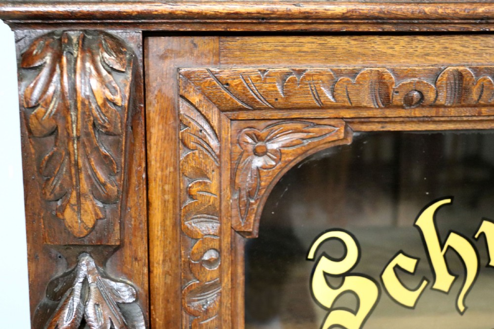 A dark carved oak side cabinet with a single glazed door displaying painted brewery signwriting and an ornate carved gallery back. View XXVII