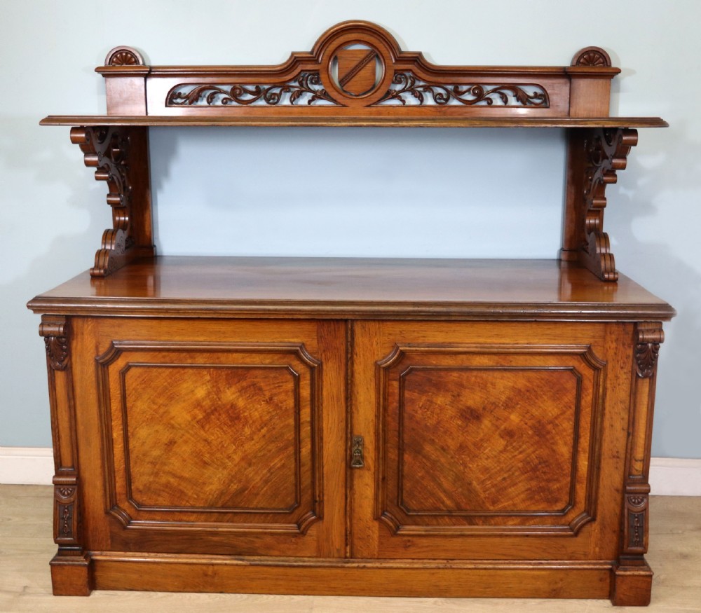 A Victorian pollard oak sideboard featuring a carved upper display shelf, fretwork cresting, and two fielded panel doors with decorative wood grain.
