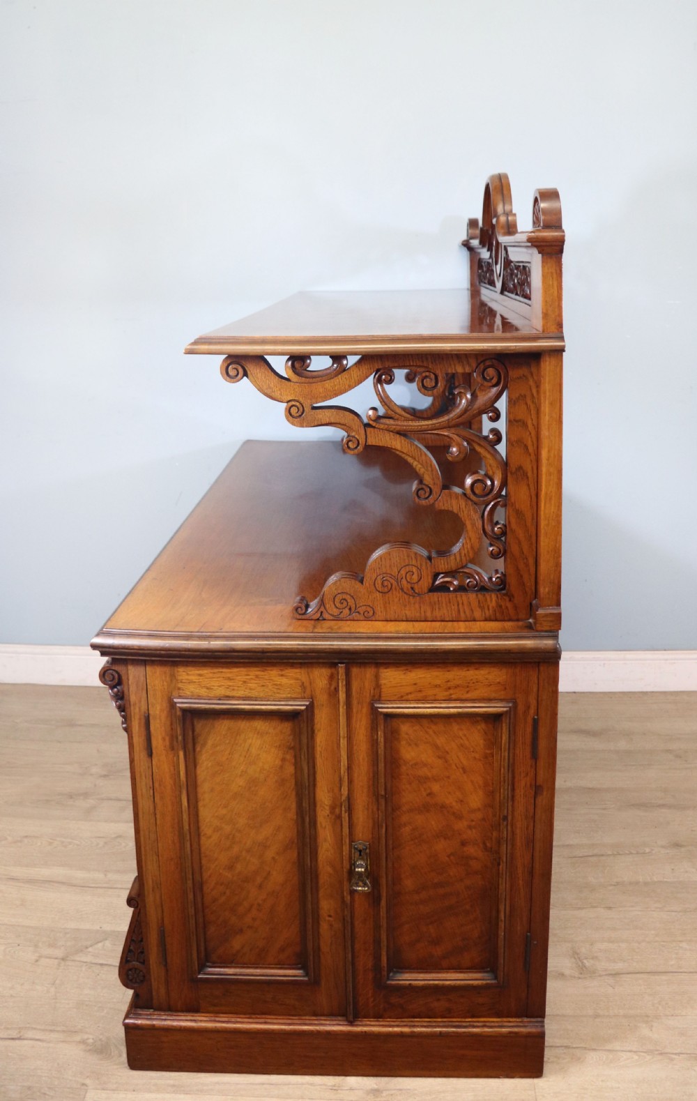A Victorian pollard oak sideboard featuring a carved upper display shelf, fretwork cresting, and two fielded panel doors with decorative wood grain. View III