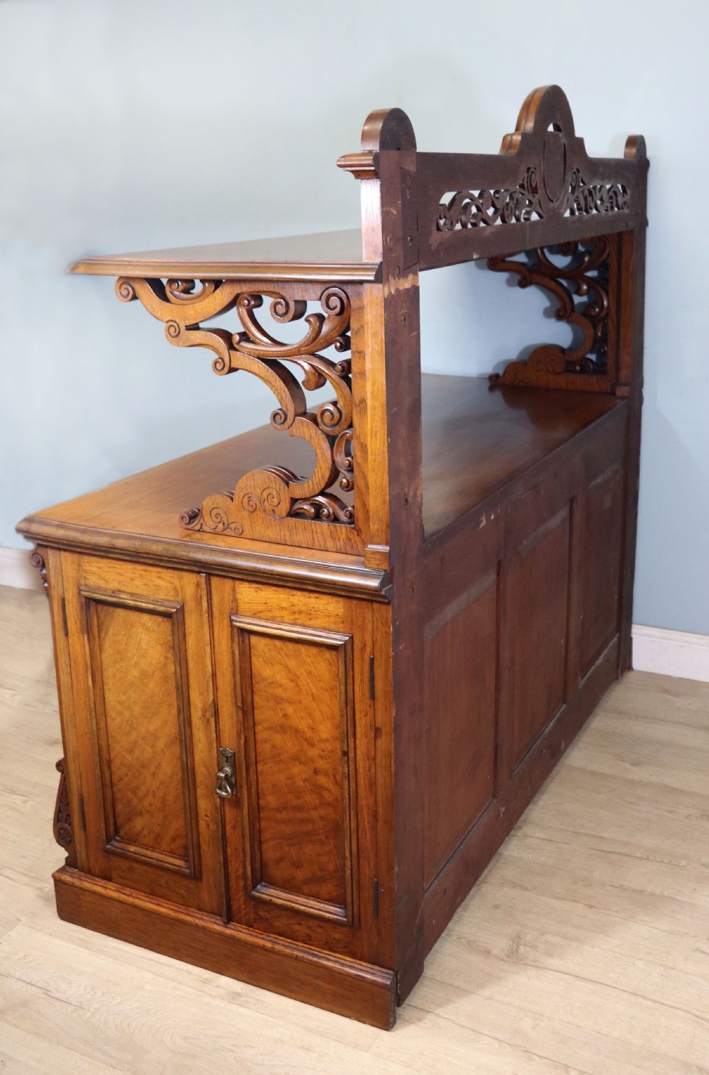 A Victorian pollard oak sideboard featuring a carved upper display shelf, fretwork cresting, and two fielded panel doors with decorative wood grain. View VI