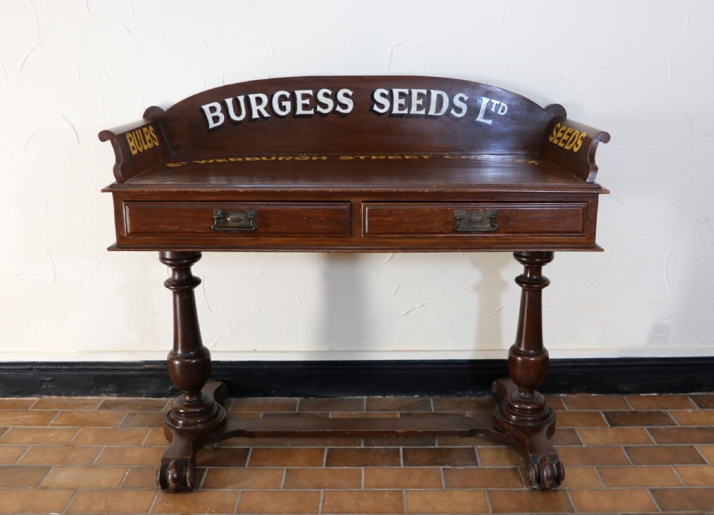 A late Victorian mahogany galleried side table featuring two drawers, turned legs on a trestle base, and painted commercial lettering.