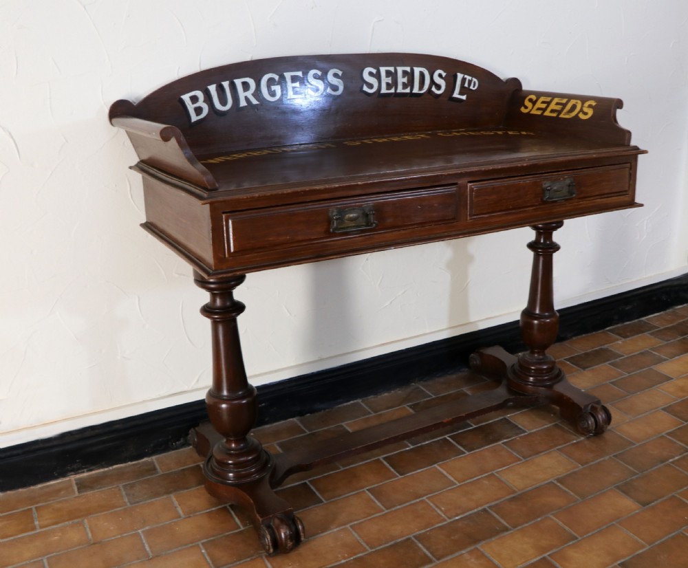 A late Victorian mahogany galleried side table featuring two drawers, turned legs on a trestle base, and painted commercial lettering. View IV