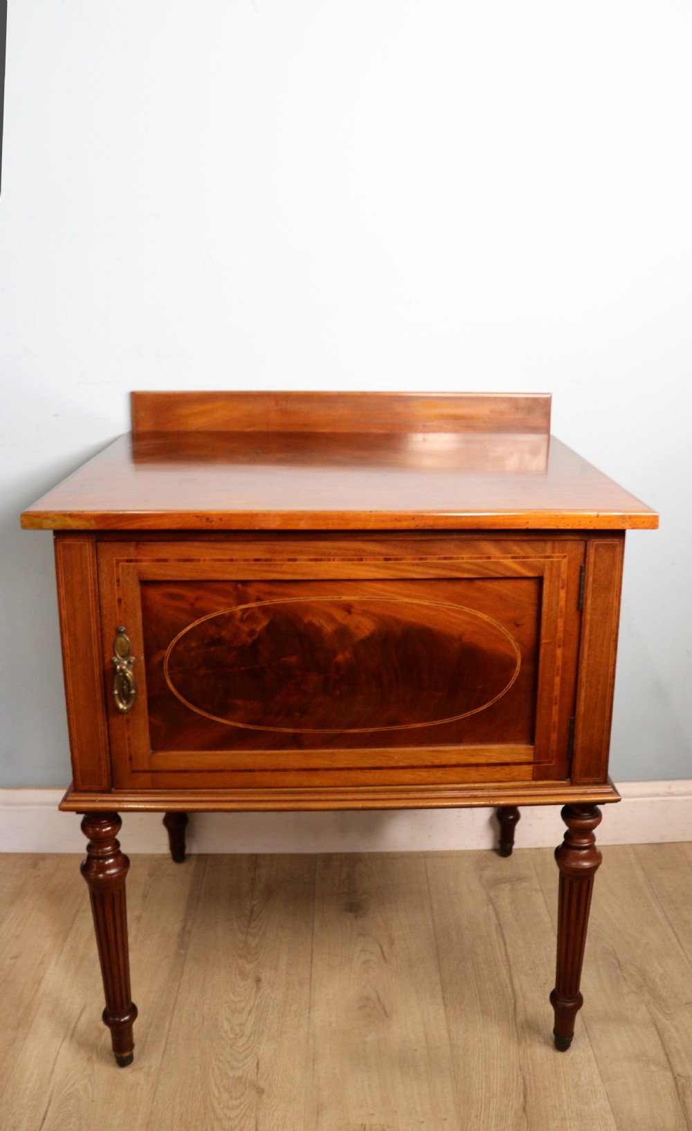 An Edwardian mahogany bedside cabinet with a single door containing a central oval marquetry inlay, raised on fluted turned legs.