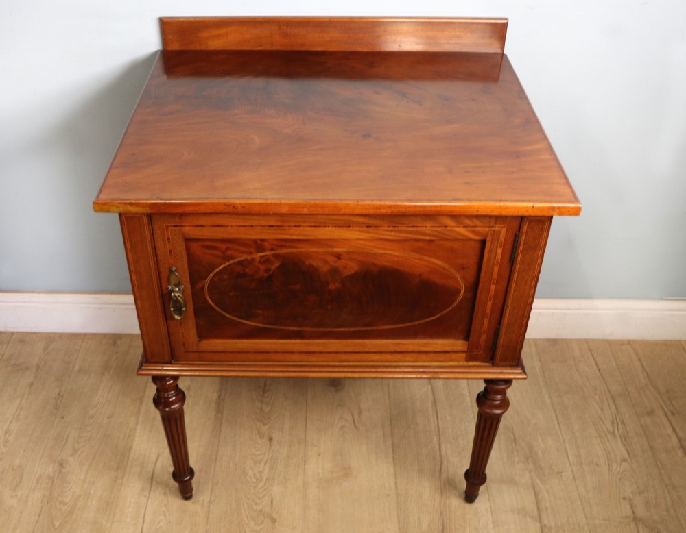 An Edwardian mahogany bedside cabinet with a single door containing a central oval marquetry inlay, raised on fluted turned legs. View III