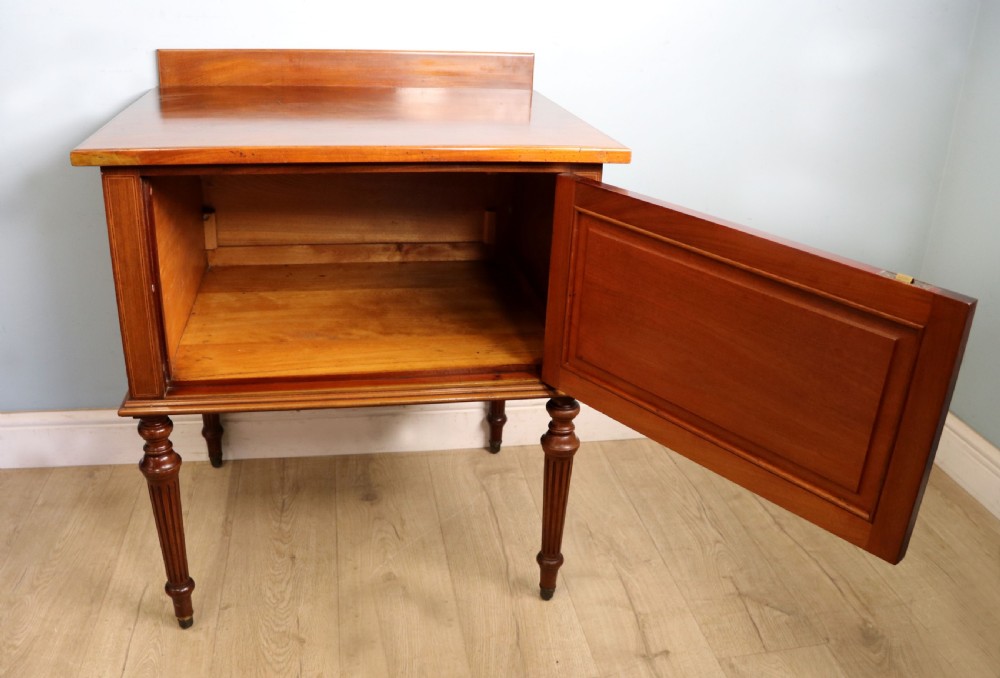An Edwardian mahogany bedside cabinet with a single door containing a central oval marquetry inlay, raised on fluted turned legs. View IV