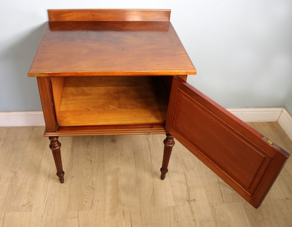 An Edwardian mahogany bedside cabinet with a single door containing a central oval marquetry inlay, raised on fluted turned legs. View V