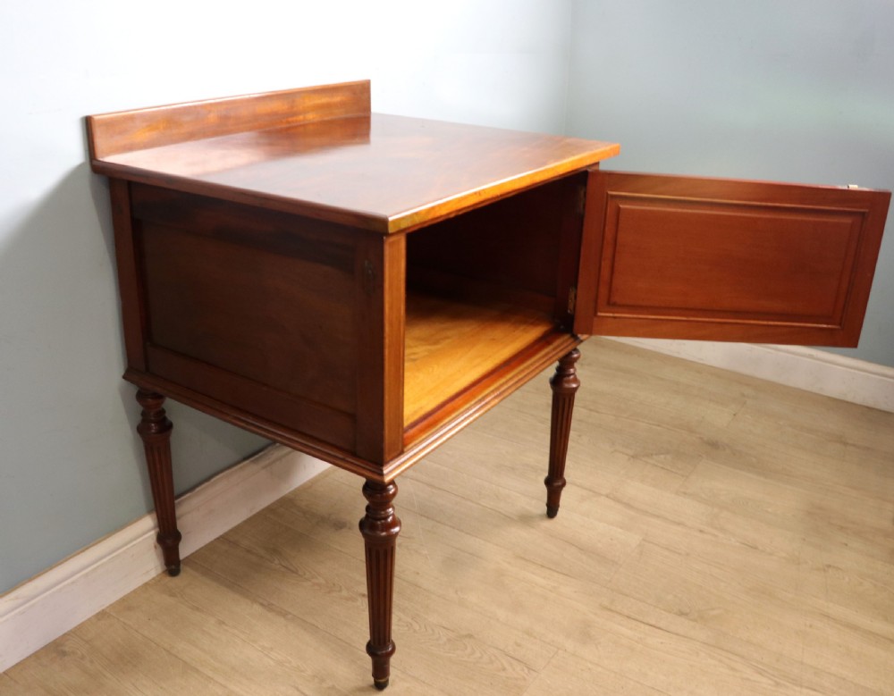 An Edwardian mahogany bedside cabinet with a single door containing a central oval marquetry inlay, raised on fluted turned legs. View VII