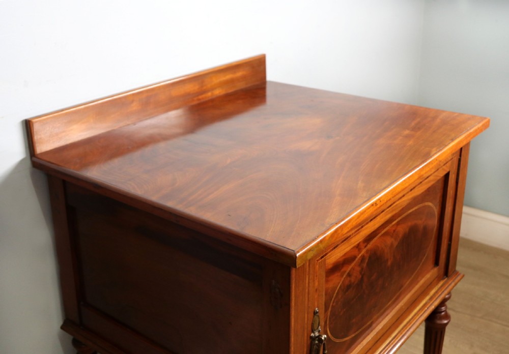 An Edwardian mahogany bedside cabinet with a single door containing a central oval marquetry inlay, raised on fluted turned legs. View X