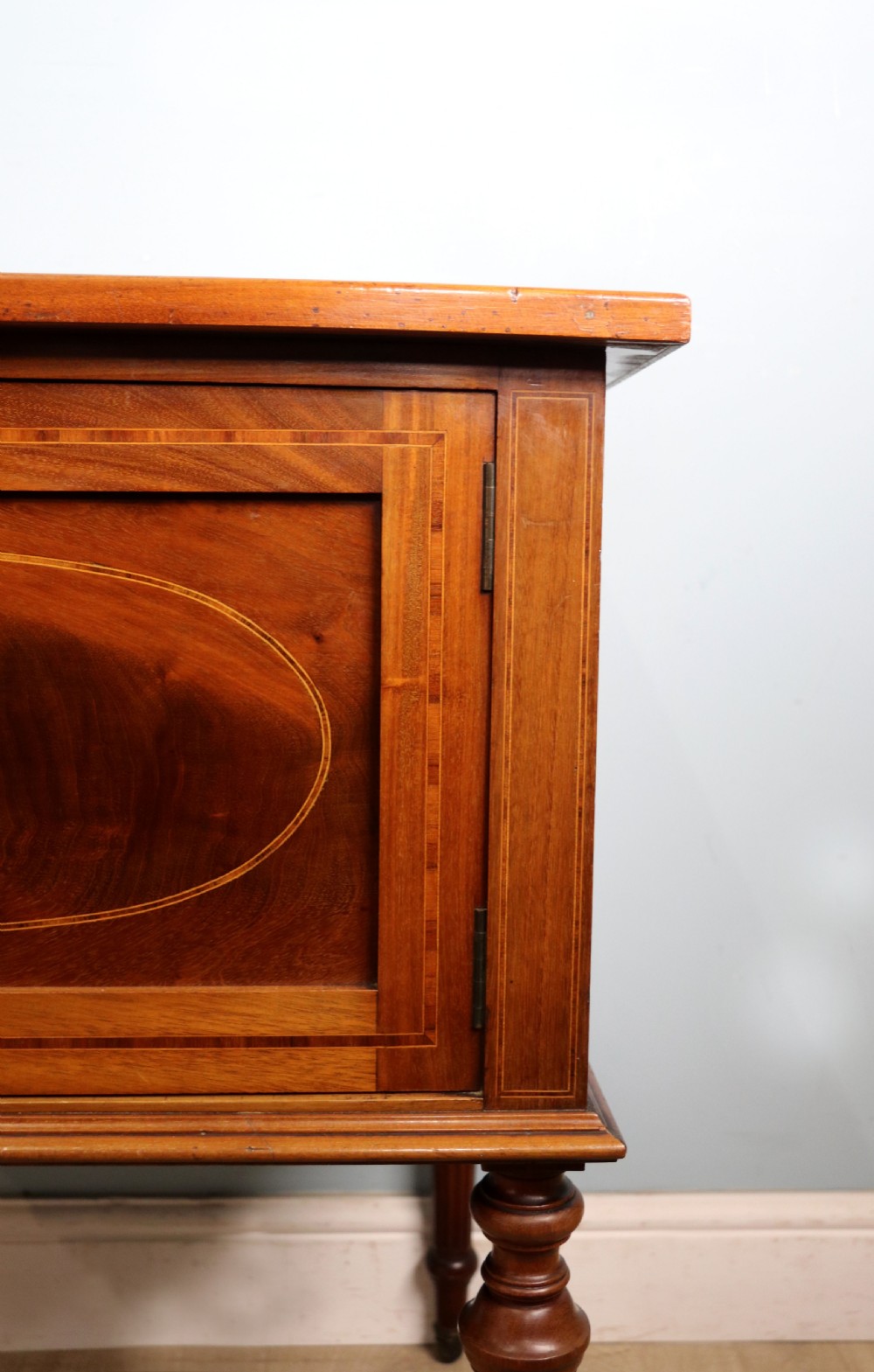 An Edwardian mahogany bedside cabinet with a single door containing a central oval marquetry inlay, raised on fluted turned legs. View XII