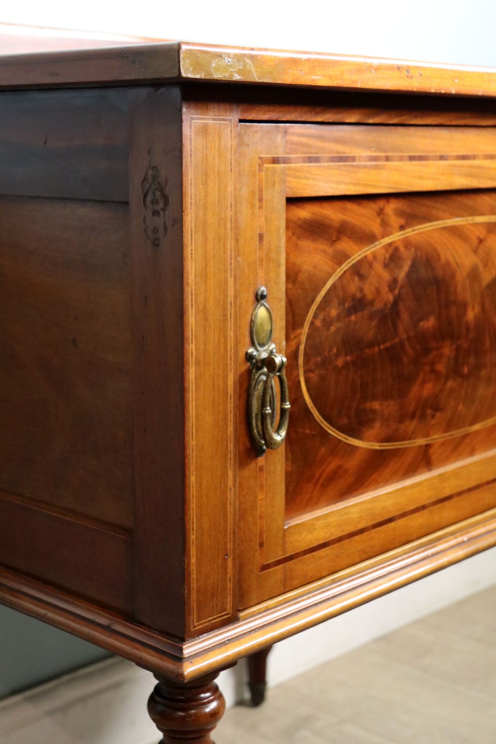 An Edwardian mahogany bedside cabinet with a single door containing a central oval marquetry inlay, raised on fluted turned legs. View XIII