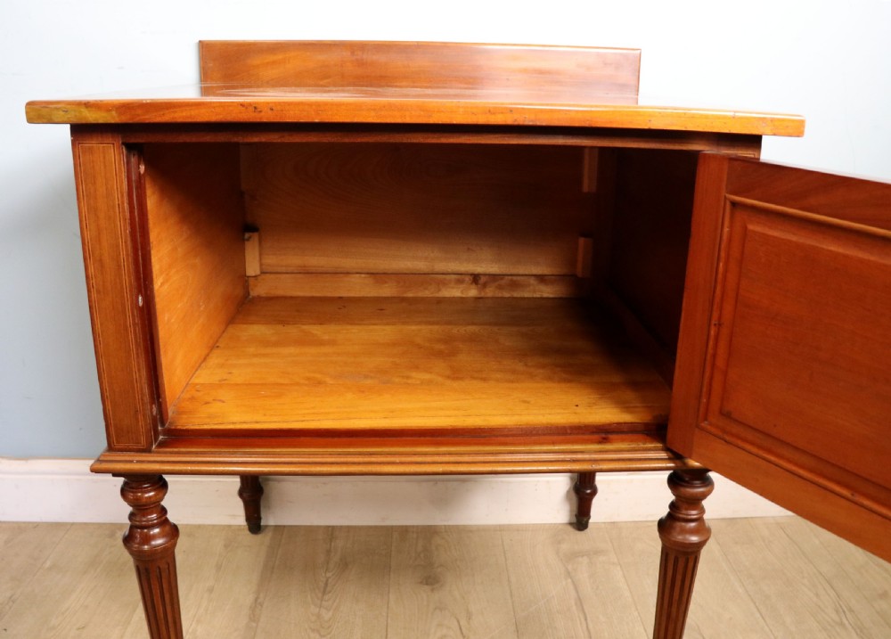 An Edwardian mahogany bedside cabinet with a single door containing a central oval marquetry inlay, raised on fluted turned legs. View XIV