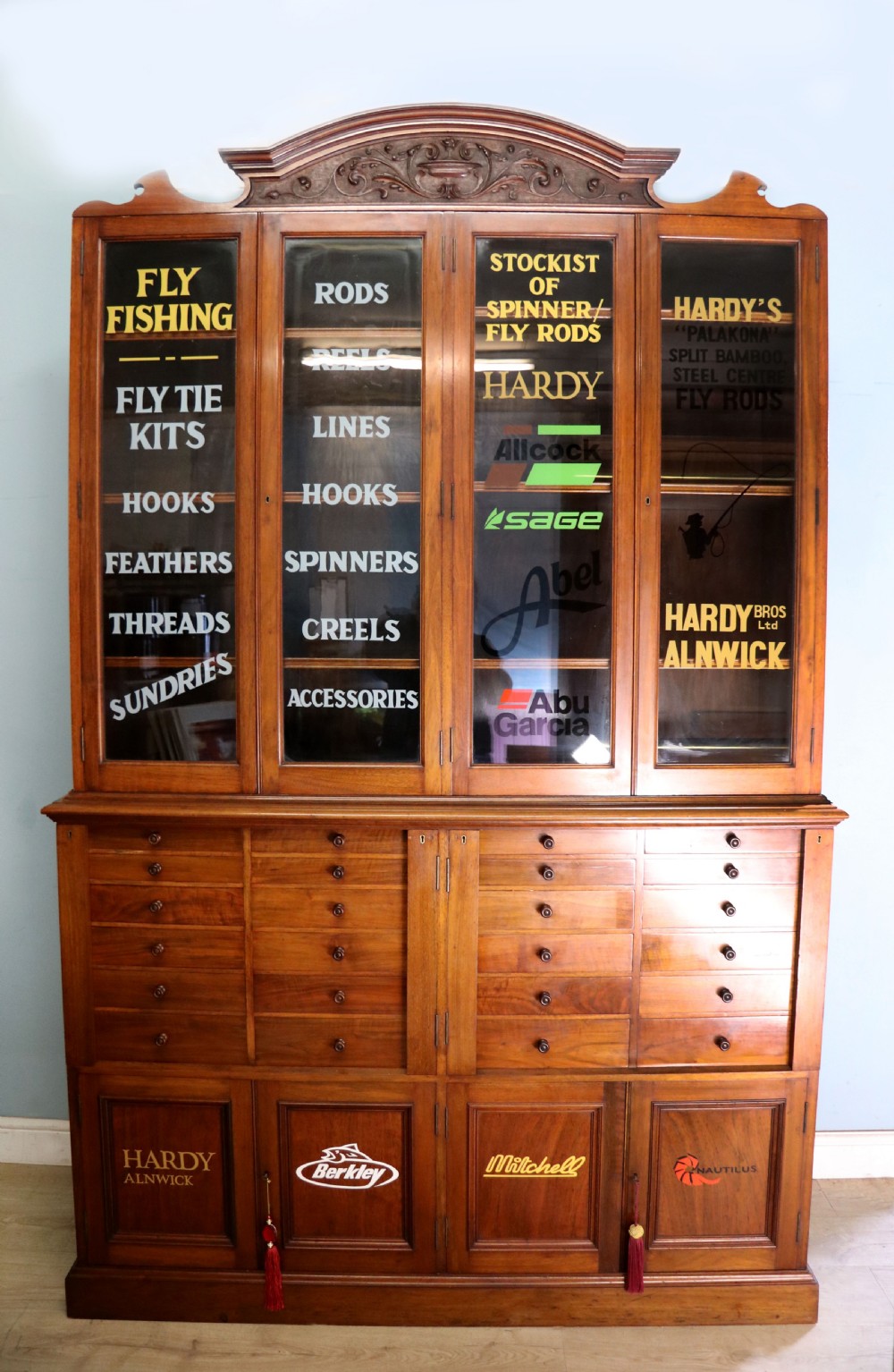 A tall Victorian solid walnut shop cabinet with glazed upper doors featuring sign-written fishing typography, multiple small drawers in the midsection, and panelled cupboard doors below.
