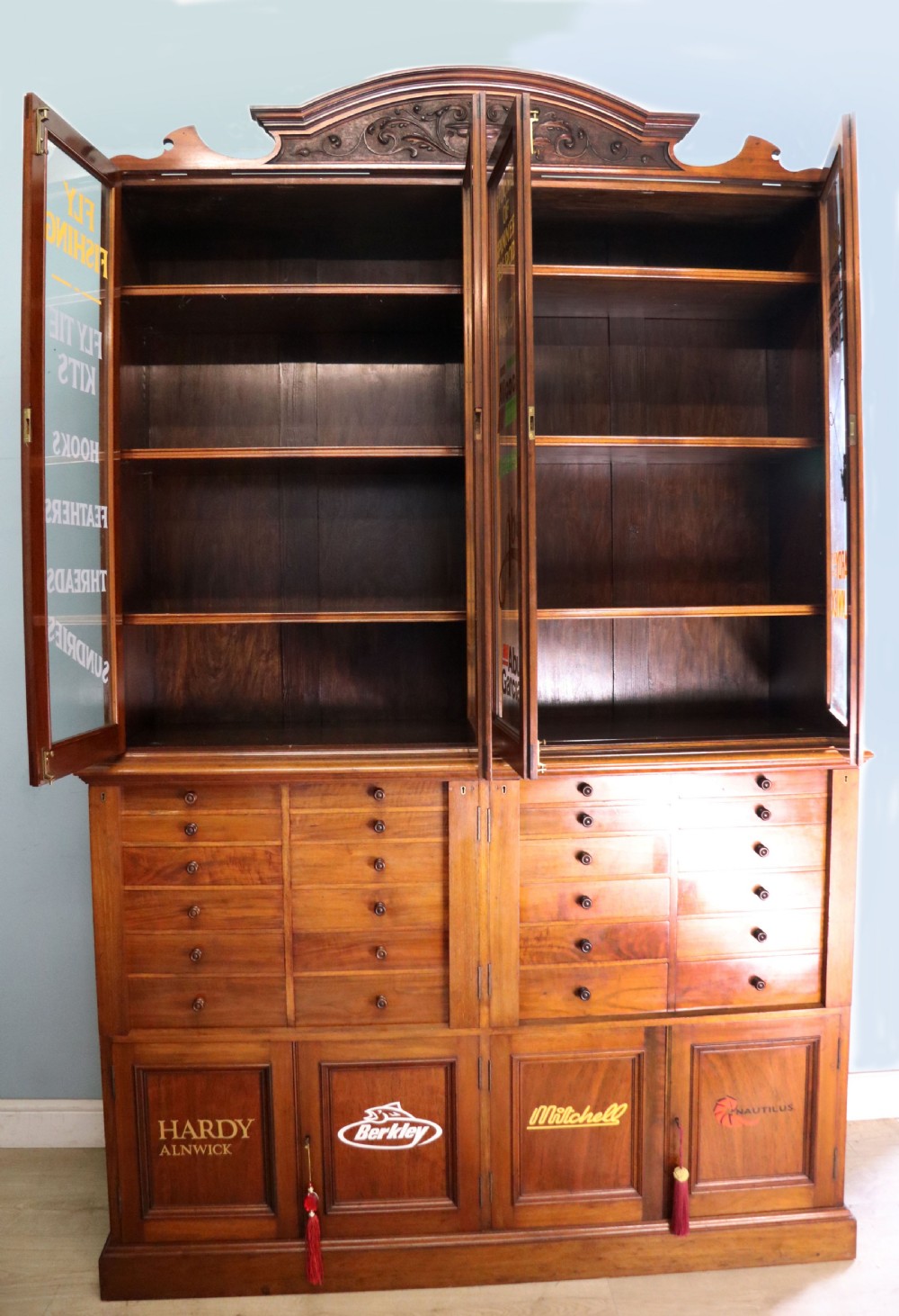 A tall Victorian solid walnut shop cabinet with glazed upper doors featuring sign-written fishing typography, multiple small drawers in the midsection, and panelled cupboard doors below. View II