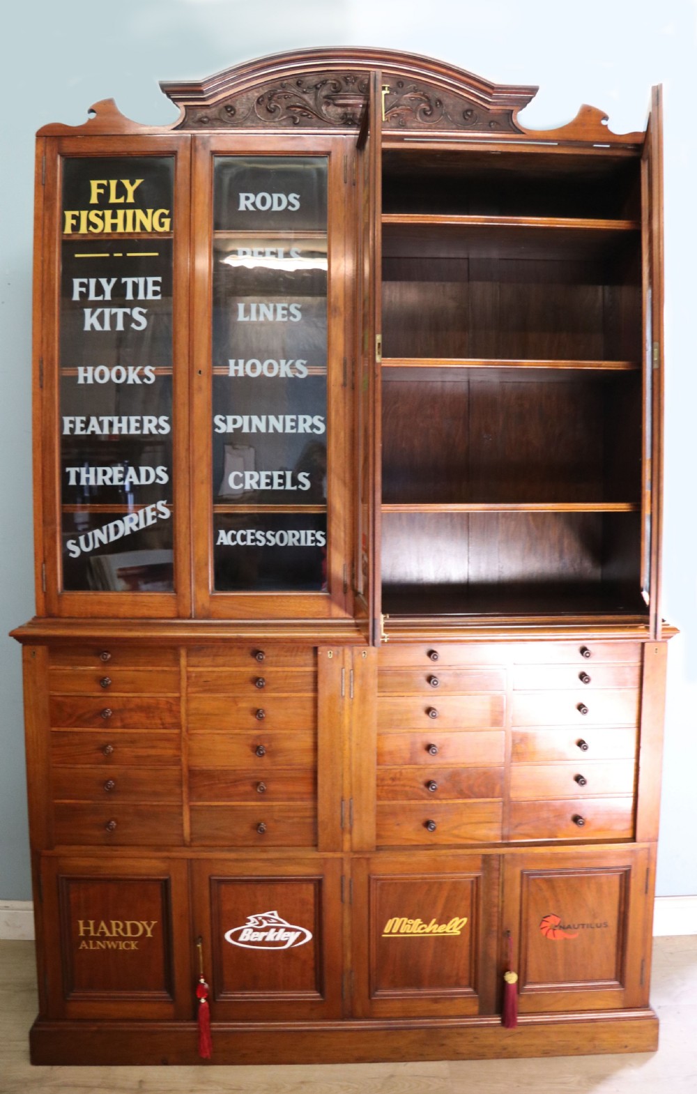 A tall Victorian solid walnut shop cabinet with glazed upper doors featuring sign-written fishing typography, multiple small drawers in the midsection, and panelled cupboard doors below. View III