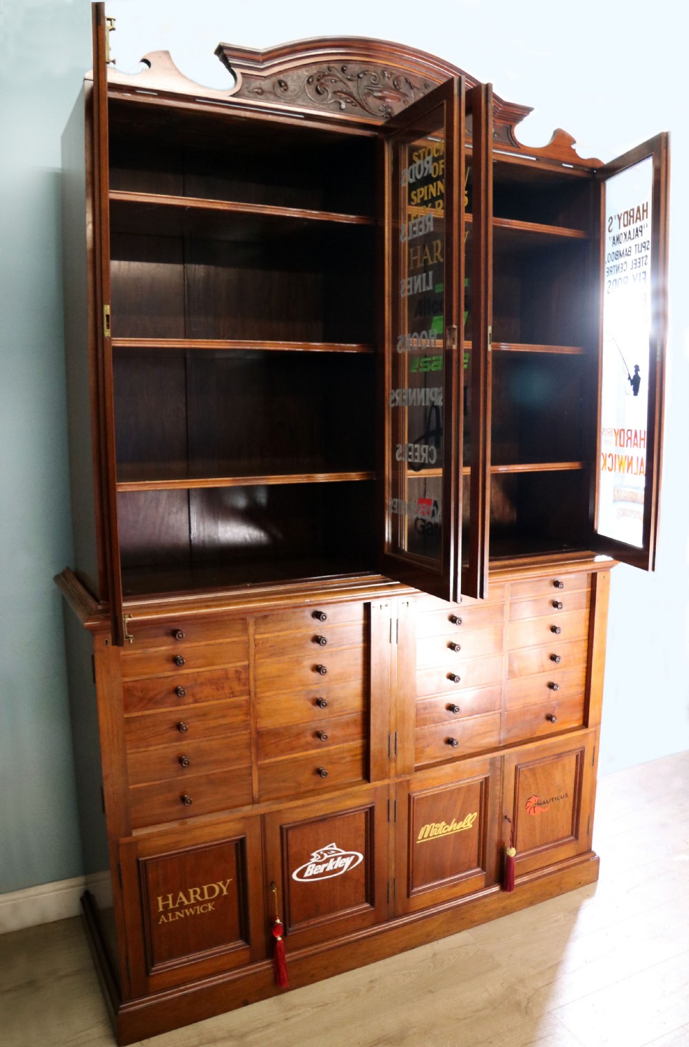 A tall Victorian solid walnut shop cabinet with glazed upper doors featuring sign-written fishing typography, multiple small drawers in the midsection, and panelled cupboard doors below. View VII