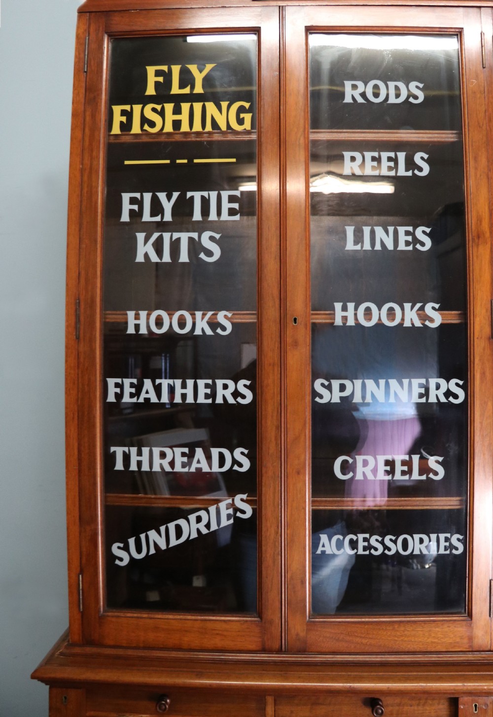 A tall Victorian solid walnut shop cabinet with glazed upper doors featuring sign-written fishing typography, multiple small drawers in the midsection, and panelled cupboard doors below. View IX