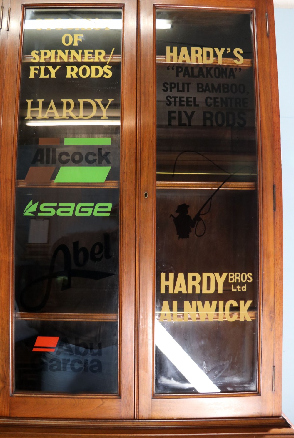 A tall Victorian solid walnut shop cabinet with glazed upper doors featuring sign-written fishing typography, multiple small drawers in the midsection, and panelled cupboard doors below. View X