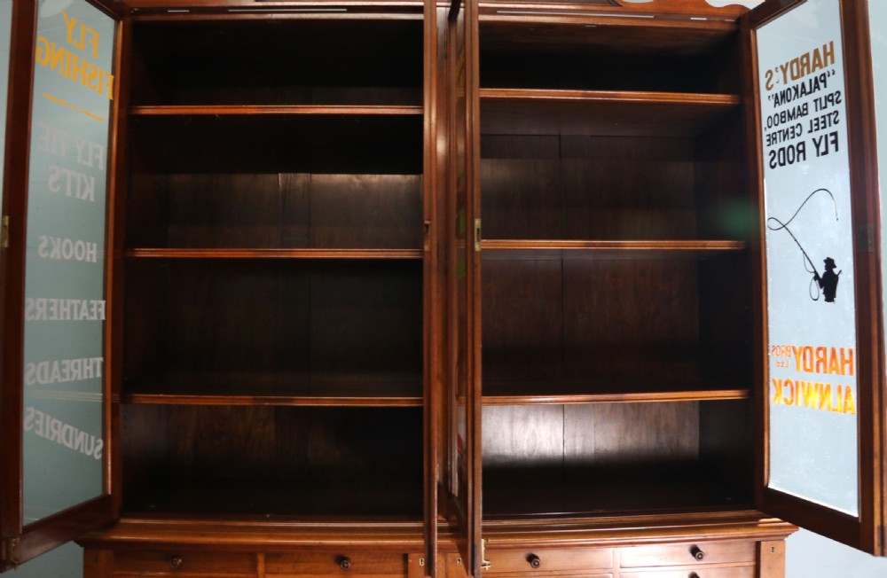 A tall Victorian solid walnut shop cabinet with glazed upper doors featuring sign-written fishing typography, multiple small drawers in the midsection, and panelled cupboard doors below. View XII