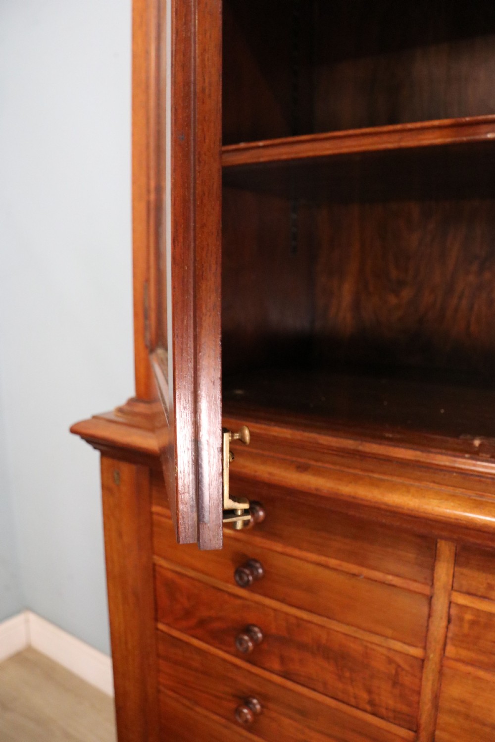 A tall Victorian solid walnut shop cabinet with glazed upper doors featuring sign-written fishing typography, multiple small drawers in the midsection, and panelled cupboard doors below. View XVI