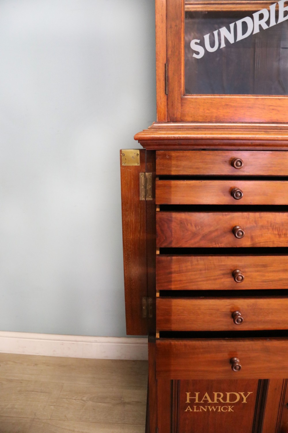 A tall Victorian solid walnut shop cabinet with glazed upper doors featuring sign-written fishing typography, multiple small drawers in the midsection, and panelled cupboard doors below. View XXI