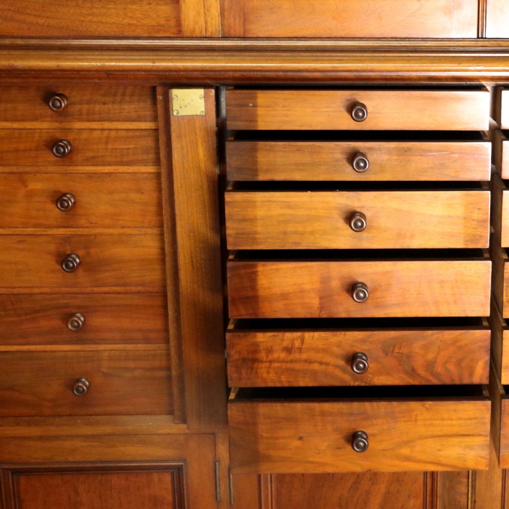 A tall Victorian solid walnut shop cabinet with glazed upper doors featuring sign-written fishing typography, multiple small drawers in the midsection, and panelled cupboard doors below. View XXIV