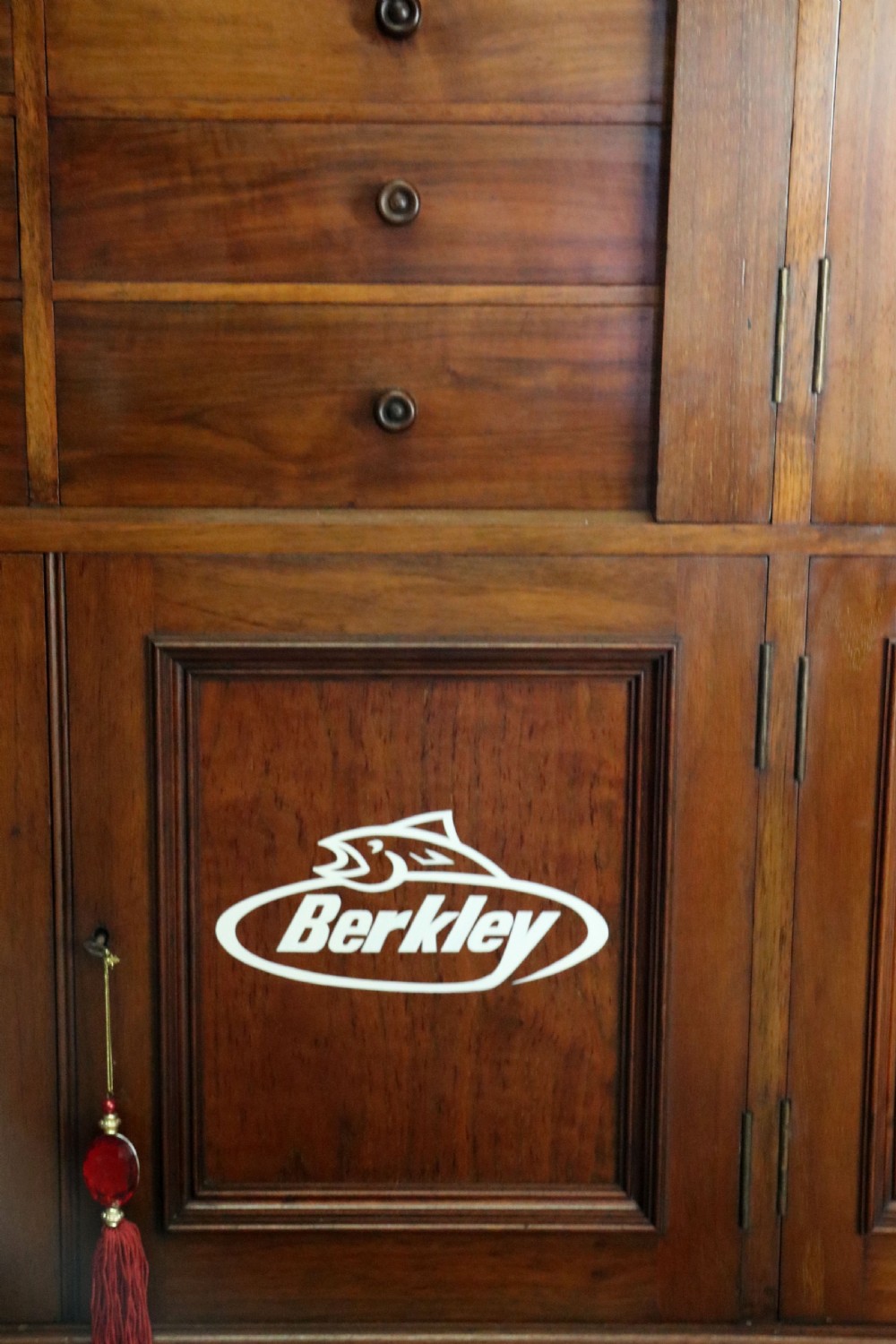 A tall Victorian solid walnut shop cabinet with glazed upper doors featuring sign-written fishing typography, multiple small drawers in the midsection, and panelled cupboard doors below. View XXX