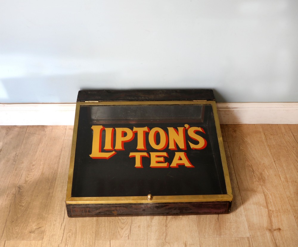 A low profile glass countertop display cabinet with a brass frame and yellow and red lettering reading Liptons Tea on a black background. View III